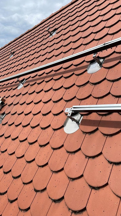 PV-Dachziegel Typ Biberschwanz im montierten Zustand: Aluminium-PV-Halterungen und Montageschienen auf rotem Biberschwanz-Dach zur Photovoltaik-Installation.